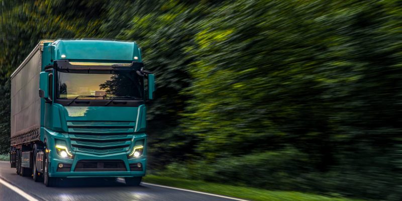 A powerful emerald green truck driving fast through a forest road, symbolizing innovation, energy, and modern logistics strength.